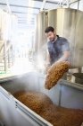 Worker in brewery, emptying grains from mash tun — Stock Photo