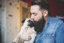 Молодой бородатый мужчина целует собаку на руках — стоковое фото