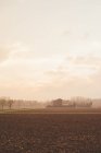 View of ploughed fields and distant farm buildings in mist — Stock Photo