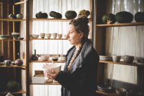Вид збоку молодої жінки, що тримає керамічну тарілку перед полицями, що показує глиняні горщики та гарбузи — стокове фото