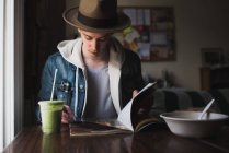 Молодой человек сидит за столом, ест, читает журнал — стоковое фото