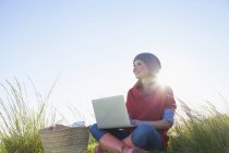 Молода жінка сидить у довгій траві, використовуючи ноутбук — стокове фото