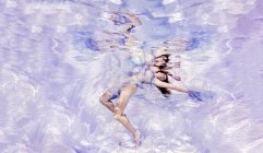 Підводний вигляд жінки, притягнутої до чистої тканини, плаває до поверхні води — стокове фото