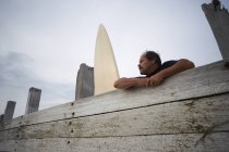 Серфер, що спирається на дерев'яний паркан з дошкою для серфінгу — стокове фото