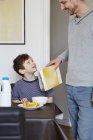 Отец наливает хлопья в миску для завтрака сына — стоковое фото