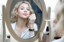 Adolescente regardant dans le miroir, appliquant le maquillage — Photo de stock