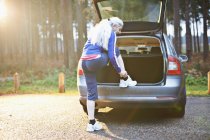 Зрелая женщина надевает кроссовки на багажник автомобиля — стоковое фото