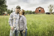Paar auf Bauernhof im hohen Gras blickt lächelnd in die Kamera, Kuss auf die Wange — Stockfoto