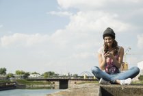 Молода жінка сидить на стіні за допомогою мобільного телефону — стокове фото