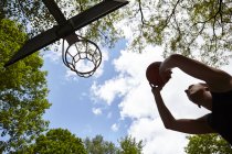 Visão de baixo ângulo de jovem silhueta apontando bola no aro de basquete — Fotografia de Stock