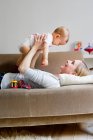 Mother lying on sofa, holding baby girl in air — Stock Photo