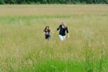 Madre e hija paseando por un largo campo de hierba - foto de stock