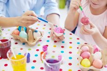 Cortado tiro de mujer e hija pintando huevos de Pascua en la mesa - foto de stock