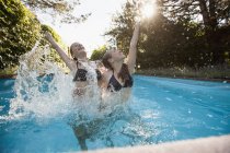Zwei Teenager springen mit erhobenen Armen in Swimmingpool — Stockfoto