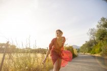 Jovem feliz vestindo vestido vermelho correndo na estrada rural, Maiorca, Espanha — Fotografia de Stock