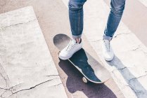 Legs and feet of young male skateboarder on pedestrian crossing — Stock Photo