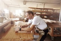 Vista lateral del hombre carpintero insertando clavija de madera en el banco de trabajo - foto de stock