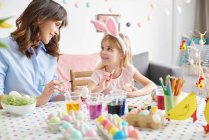 Ragazza e madre pittura uova di Pasqua a tavola — Foto stock