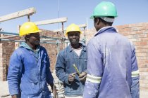 Constructores africanos hablando en el sitio de construcción - foto de stock