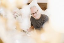 Homme âgé souriant et lisant le journal au lit — Photo de stock