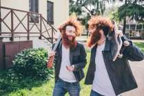 Jovens gêmeos hipster skate masculino com barbas vermelhas passeando no parque — Fotografia de Stock