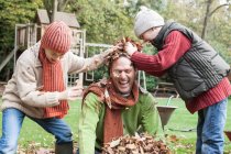 Padre e figli che giocano in giardino, lanciando foglie autunnali — Foto stock