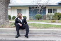Ragazzo in giacca e cravatta seduto sulla strada suburbana — Foto stock