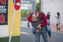 Medio hombre adulto dando a cuestas a su novia en la calle de la ciudad - foto de stock