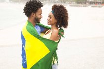 Casal sorridente envolto em bandeira brasileira na praia de Ipanema, Rio de Janeiro, Brasil — Fotografia de Stock
