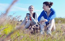 Two young women sitting on grass, drinking and talking — Stock Photo