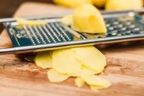 Potato with grater on wooden board — Stock Photo