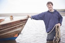 Porträt eines Mannes, der ein Seil hält und sich an ein Ruderboot lehnt — Stockfoto