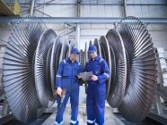 Engineers discussing notes in front of steam turbine in workshop — Stock Photo