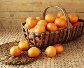 Panier vintage rempli de mandarines sur tissu — Photo de stock