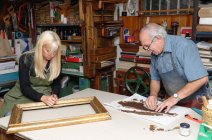 Senior man and young woman restoring picture frame and book spine in traditional bookbinding workshop — Stock Photo