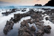 Formações rochosas de lava na praia durante o pôr do sol — Fotografia de Stock
