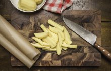 Top view of peeled and sliced potatoes, kitchen knife on chopping board — Stock Photo