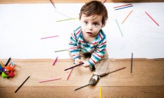 Вид сверху на мальчика, сидящего на полу с цветными карандашами и длинной бумагой — стоковое фото