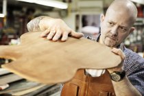 Производитель гитары проверяет деревянную гитару в мастерской — стоковое фото