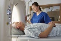 Female radiographer reassuring man going into CT scanner — Stock Photo