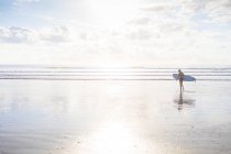 Vue lointaine de la femme portant une planche de surf sur la plage, Nosara, Province de Guanacaste, Costa Rica — Photo de stock