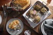 Dish of chicken pie with portion and roasted lamb racks on table — Stock Photo