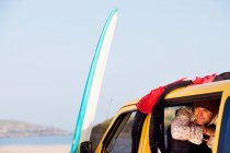 Hombre en furgoneta sonriendo con tabla de surf - foto de stock