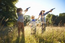 Trois petits garçons habillés en cow-boys tenant des pistolets jouets — Photo de stock