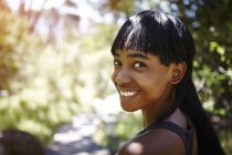 Portrait of young woman, outdoors, looking over shoulder, smiling — Stock Photo