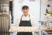 Boulanger femelle portant plateau de pâtisseries dans la cuisine — Photo de stock