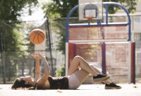 Jeune femme allongée sur le terrain de basket lancer ballon — Photo de stock