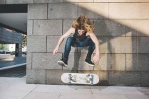 Молодой городской скейтбордист делает трюк со скейтбордом над скейтбордом — стоковое фото