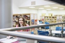 Giovane donna che lavora in biblioteca, sorridente e distogliendo lo sguardo — Foto stock