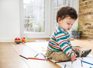Male toddler sitting on floor drawing on long paper — Stock Photo
